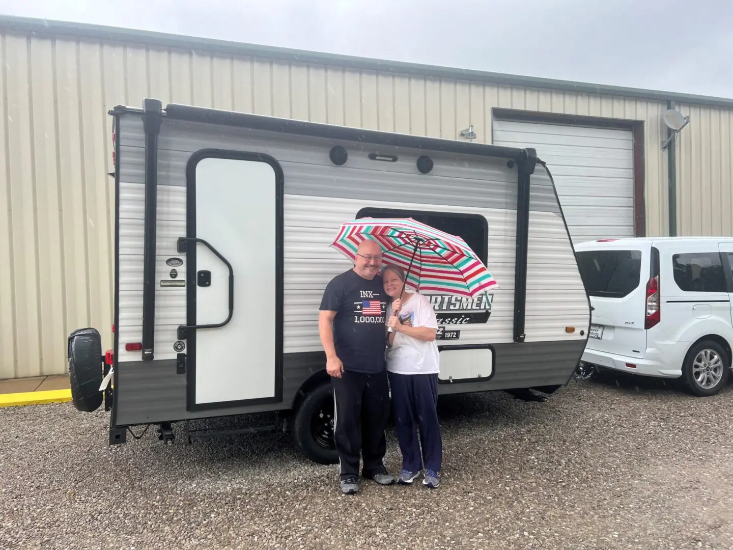 Couple with umbrella beside small camper