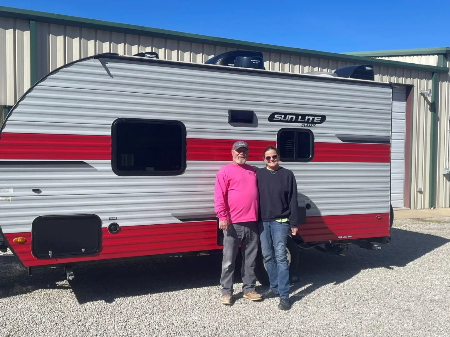 Two individuals beside a parked camper